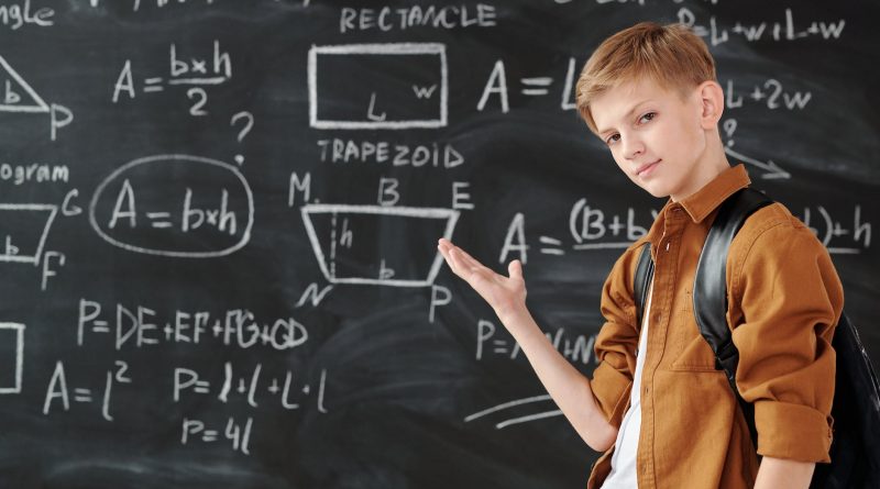 boy in brown jacket standing in front of chalk board